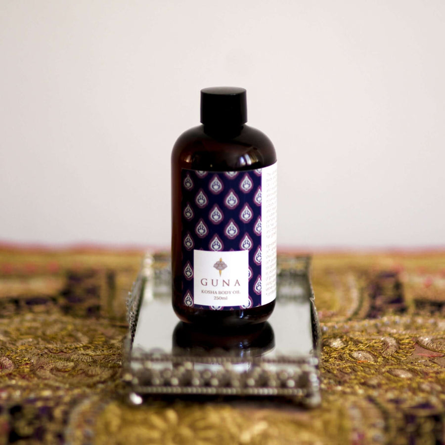A bottle of Guna's Kosha Body Oil sitting on a mirror tray
