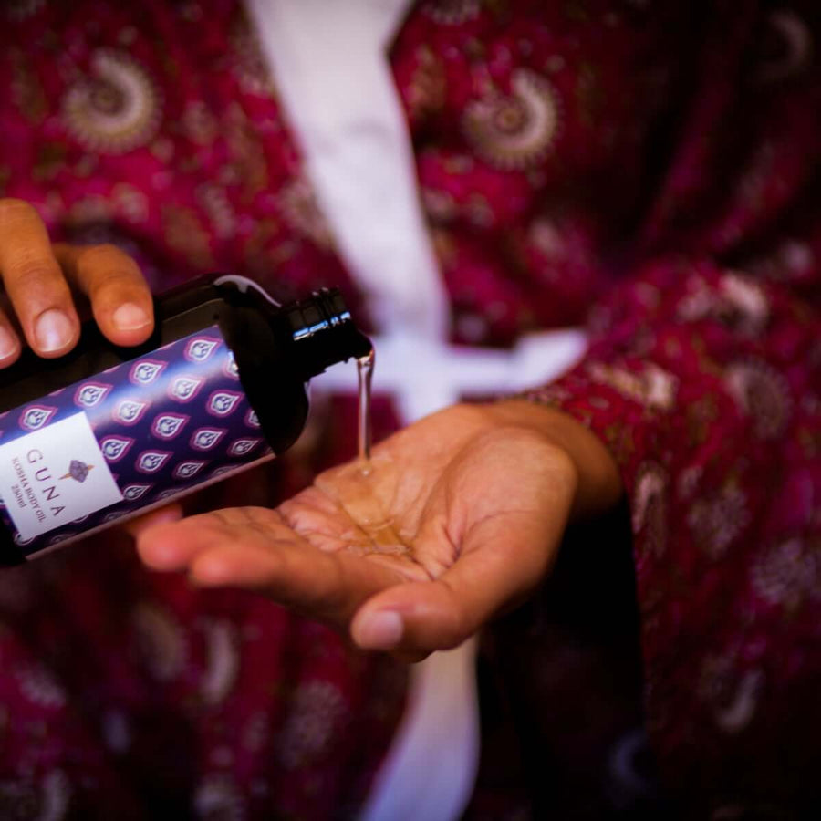 An Indian woman holding Guna's Kosha Body oil in one hand and pouring it into her other palm