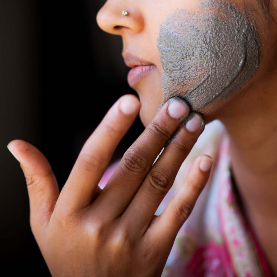 A close up of the side of an Indian woman's face with the Vajara Scrub being massaged into her cheek with her hand