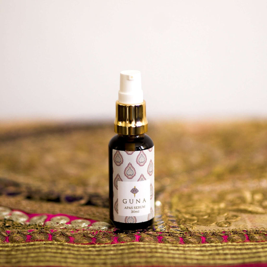 A 30ml bottle of Guna's Apas Serum, with a white label with a dark red and green pattern on it 