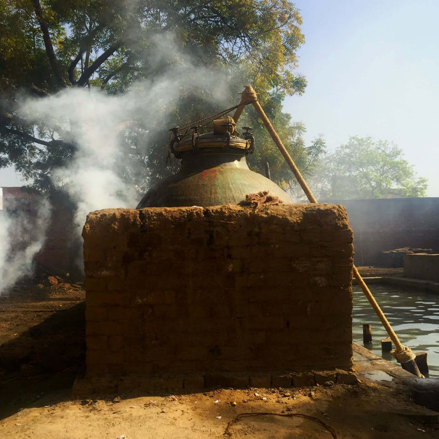 A deg and bhapka, Indian copper distillation pot and pipe, in Hathras, India, with smoke around it as it steam-distills aromatic materials into perfume