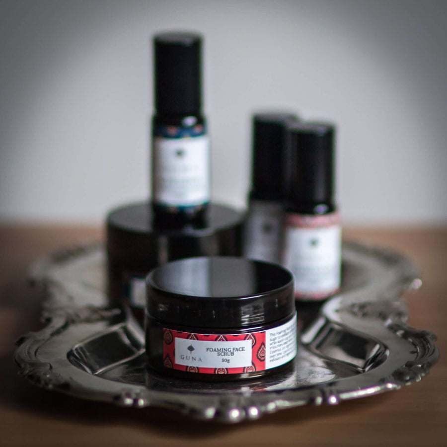 A jar of Guna's Vajara Scrub sitting on a silver tray with other Guna products behind it