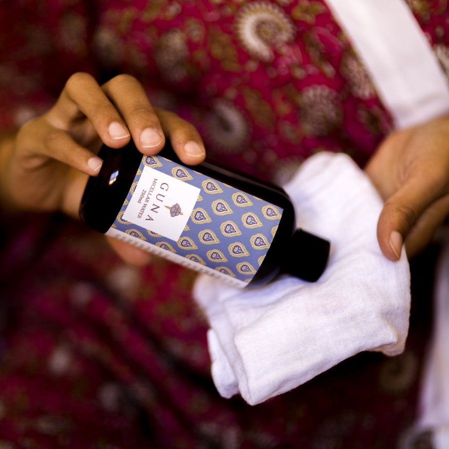 An Indian woman holding a bottle of Micellar Water and pouring some onto a Muslin Washcloth