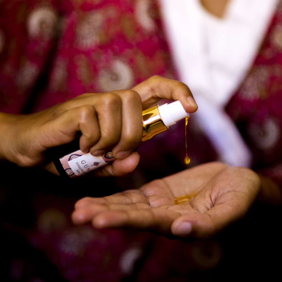 An Indian woman holding a bottle of Guna's Soma Face Oil, pumping the liquid gold coloured oil into her other palm