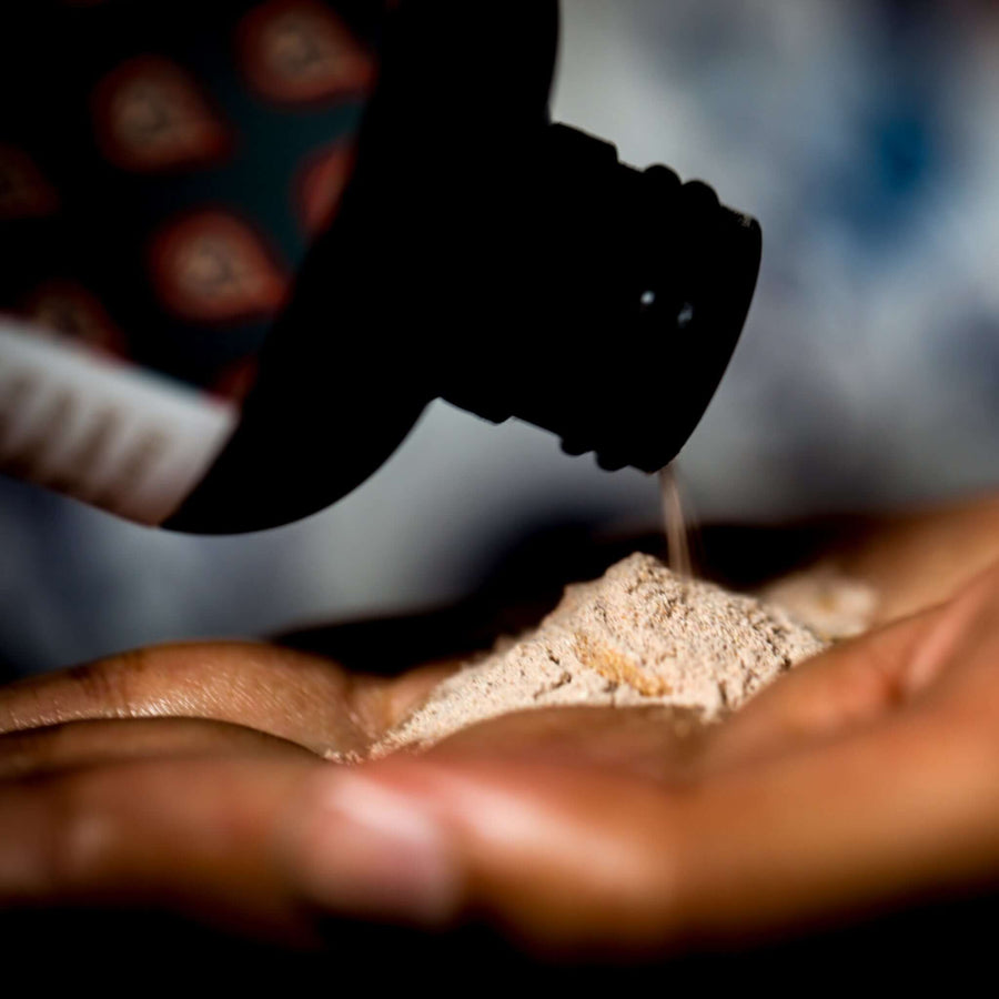 A close up of Guna's Ubtan powder cleanser being poured from the bottle into another palm