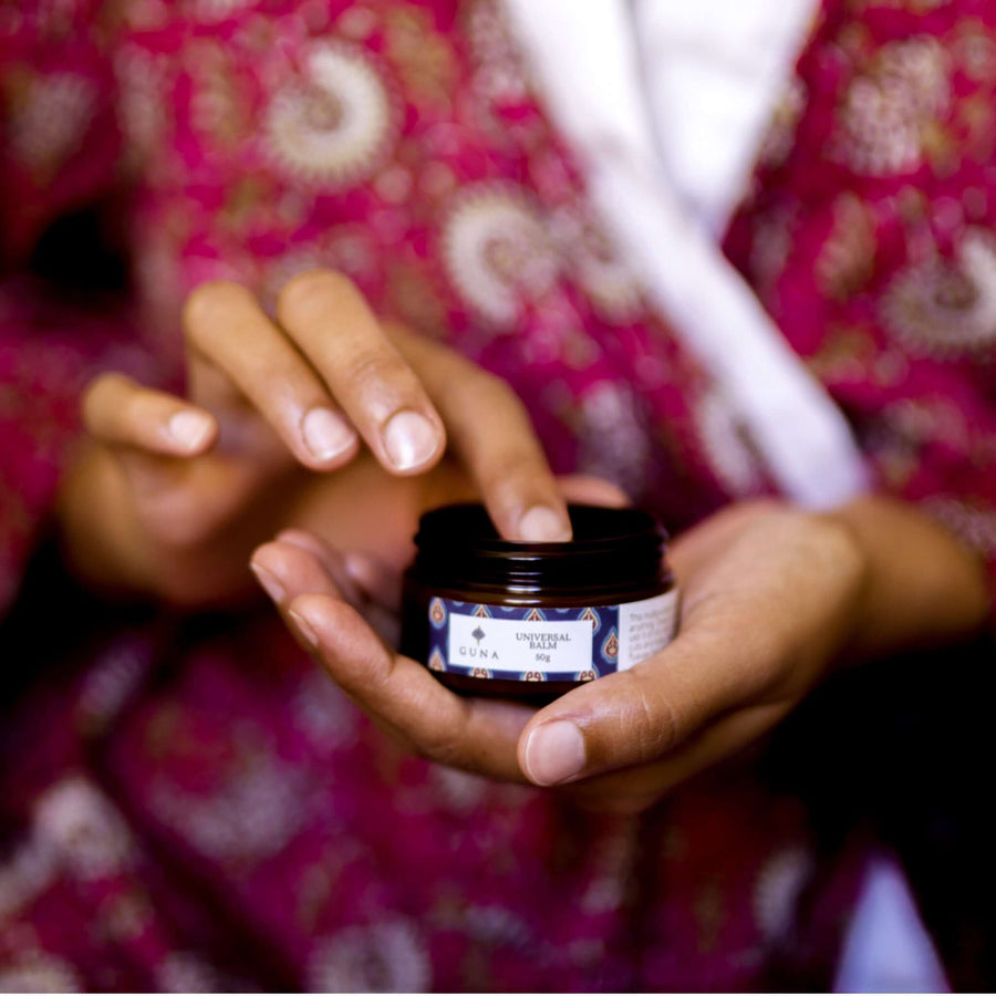 An Indian woman holding a jar of Guna's Universal Balm in one hand while scooping out a small amount with her other hand