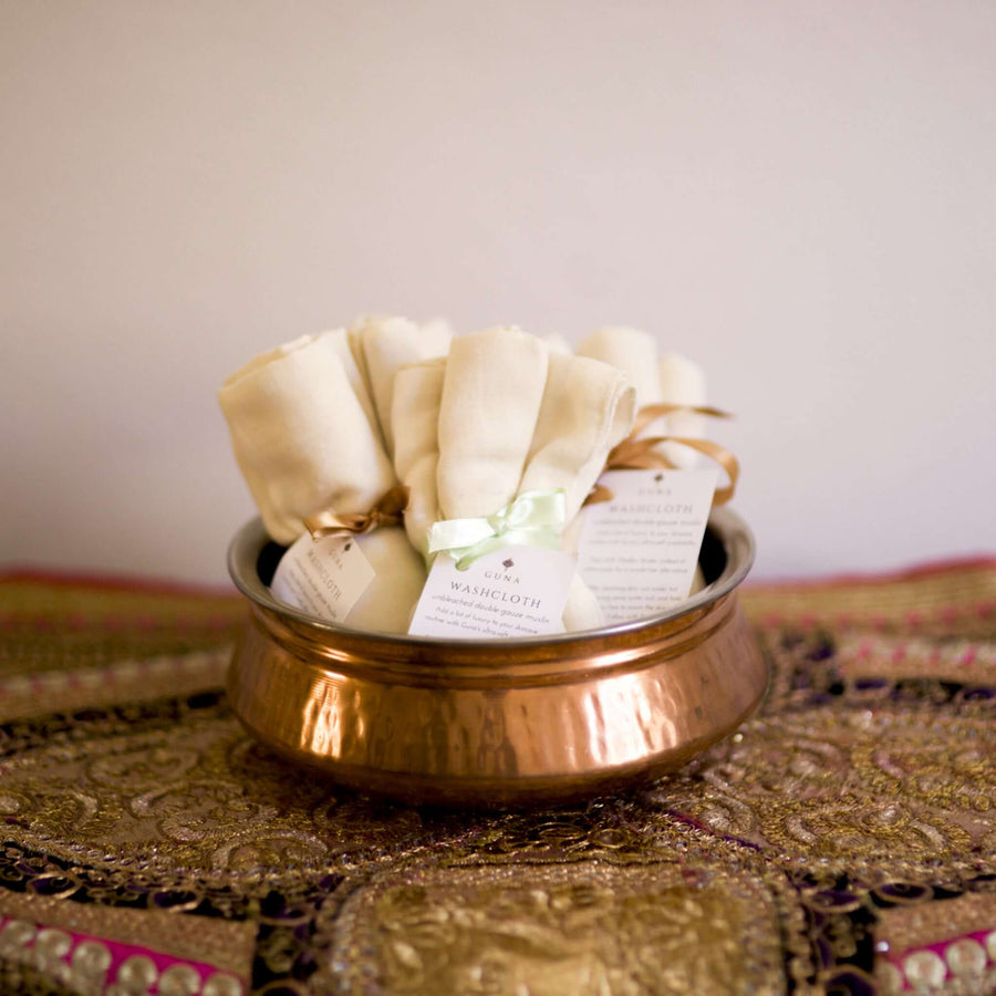 Guna's Muslin Washcloths rolled up and tied with ribbons, placed within a hand-beaten copper bowl